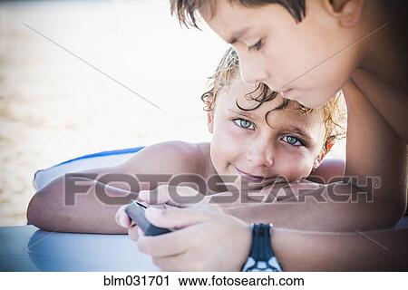 Stock Image - Boys playing with cell phone together outdoors. Fotosearch