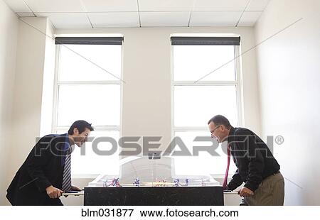 Businessmen playing foosball together in office View Large Photo Image Stock Photo - Businessmen playing foosball together in office. Fotosearch