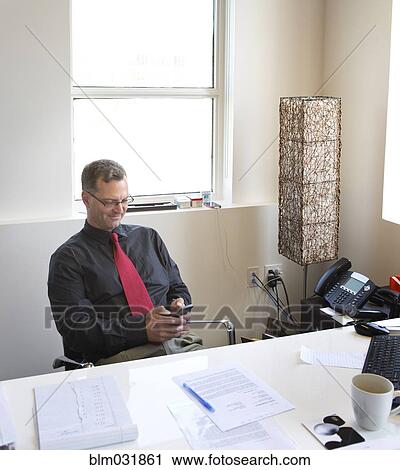 Stock Image - Caucasian businessman using cell phone in office. Fotosearch