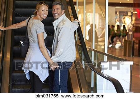 Stock Photography - Caucasian couple riding escalator in shopping mall. Fotosearch