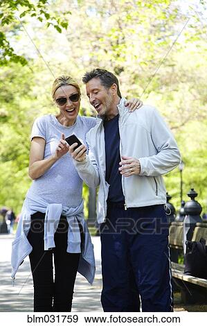 Stock Photo - Caucasian couple using cell phone in park. Fotosearch