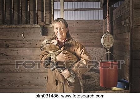 Stock Photograph - Caucasian farmer holding lamb in barn. Fotosearch