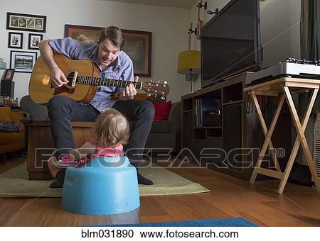 Stock Image - Caucasian father playing guitar for daughter. Fotosearch