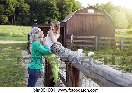 Stock Image - Caucasian grandmother and granddaughter smiling at farm fence. Fotosearch