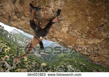 Stock Image - Climber hanging from rock formation. Fotosearch