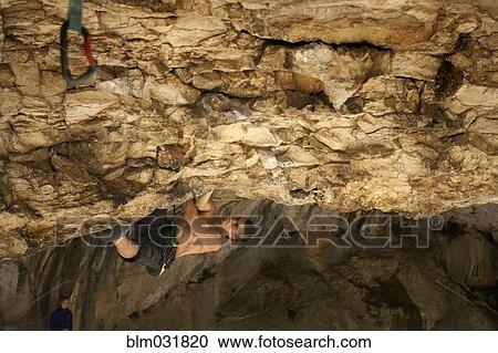Stock Image - Climber hanging from rocky cave ceiling. Fotosearch