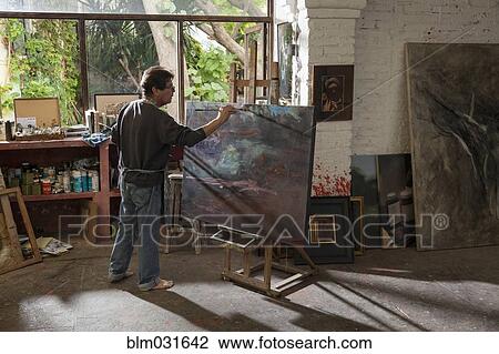 Stock Image - Hispanic artist painting in studio. Fotosearch