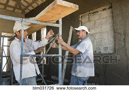 Stock Photograph - Hispanic construction workers with scaffolding at construction site. Fotosearch