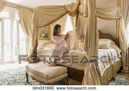 Stock Image - Hispanic woman admiring clothes on bed. Fotosearch
