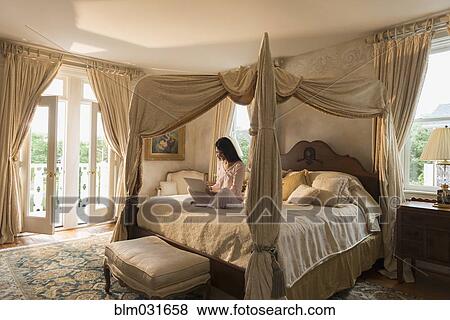 Stock Photo - Hispanic woman using laptop on bed. Fotosearch