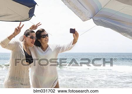 Stock Image - Hispanic women taking cell phone selfie at beach. Fotosearch