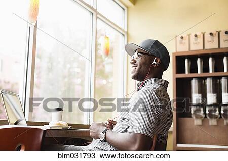 Stock Image - Laughing Black man using laptop in coffee shop. Fotosearch