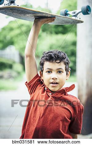 Stock Image - Mixed race boy carrying skateboard. Fotosearch