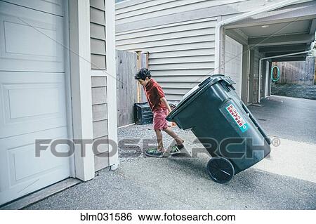 Stock Photograph - Mixed race boy pulling trash can in driveway. Fotosearch