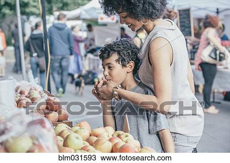 Stock Image - Mixed race boy shopping with mother at farmers market. Fotosearch