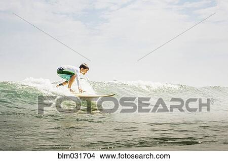 Picture - Mixed race boy surfing in waves. Fotosearch