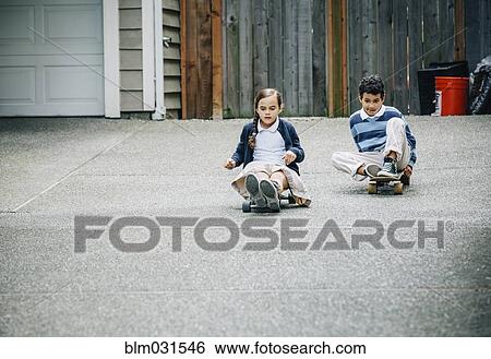 Stock Photograph - Mixed race brother and sister riding skateboards in driveway. Fotosearch
