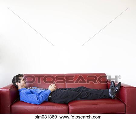 Stock Photo - Mixed race businessman using cell phone on sofa. Fotosearch