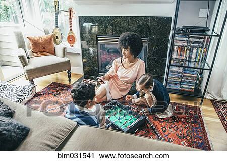 Stock Image - Mixed race family playing foosball on living room floor. Fotosearch