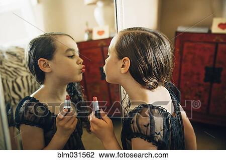 Stock Image - Mixed race girl applying lipstick in mirror. Fotosearch