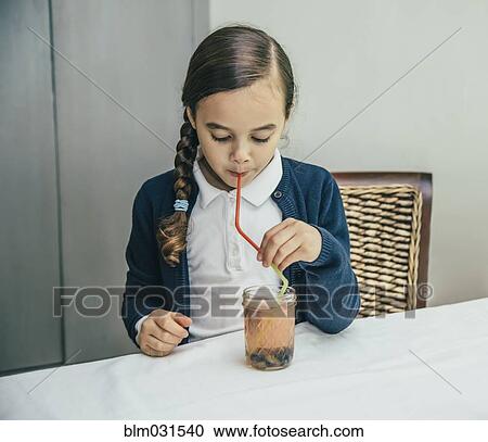 Stock Image - Mixed race girl drinking juice from jar through straw. Fotosearch
