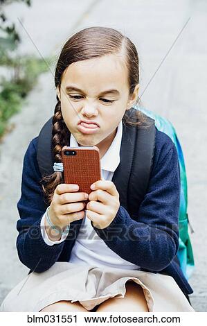 Stock Image - Mixed race girl making a face at cell phone. Fotosearch