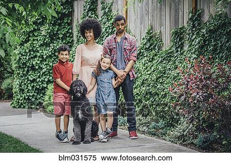 Stock Photography - Mixed race mother and children smiling with dog on suburban sidewalk. Fotosearch