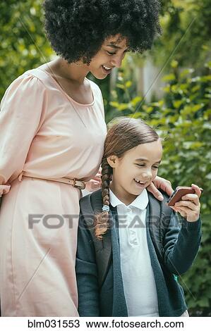 Stock Image - Mixed race mother and daughter using cell phone together. Fotosearch