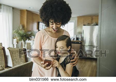 Stock Photograph - Mixed race mother and daughter using cell phone. Fotosearch