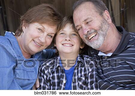 Stock Photograph - Older Caucasian couple relaxing with grandson outdoors. Fotosearch