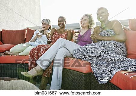 Stock Photo - Women drinking wine together on urban rooftop. Fotosearch