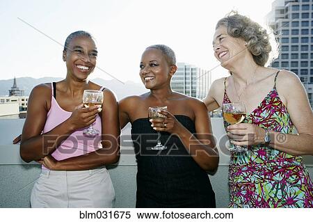 Stock Photography - Women drinking wine together on urban rooftop. Fotosearch