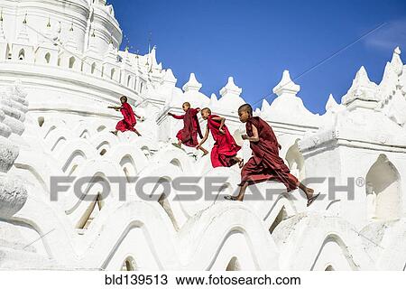 Stock Image - Asian monks running on white temple walls, Hsinbyume Pagoda, Mandalay, Sagaing, Myanmar. Fotosearch