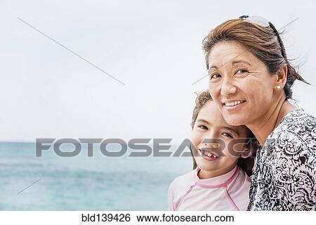 Stock Photograph - Asian mother and daughter smiling near ocean. Fotosearch