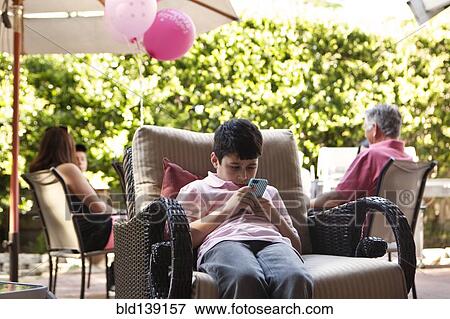 Bored boy using cell phone at party View Large Photo Image Stock Photo - Bored boy using cell phone at party. Fotosearch