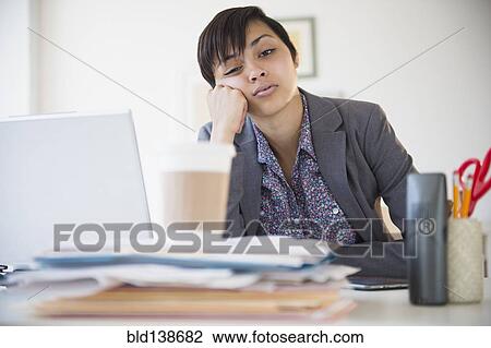 Stock Image - Bored mixed race businesswoman sitting at office desk. Fotosearch