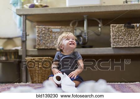 Stock Image - Caucasian baby unraveling toilet paper in bathroom. Fotosearch