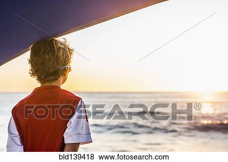 Stock Photo - Caucasian boy admiring ocean sunset. Fotosearch