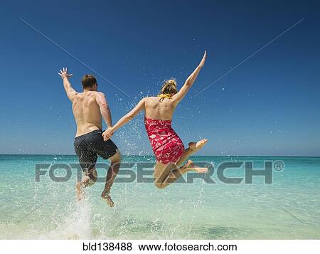Stock Photo - Caucasian couple jumping for joy in tropical ocean. Fotosearch