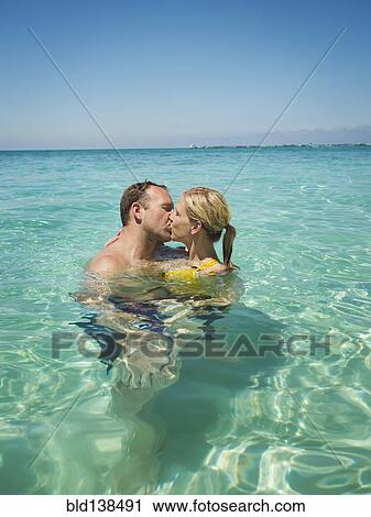 Stock Image - Caucasian couple kissing in water in tropical ocean. Fotosearch