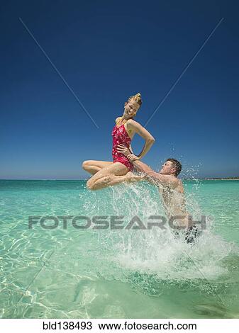 Stock Image - Caucasian couple playing in water in tropical ocean. Fotosearch