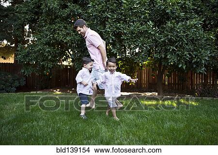 Picture - Caucasian father and sons playing in backyard. Fotosearch