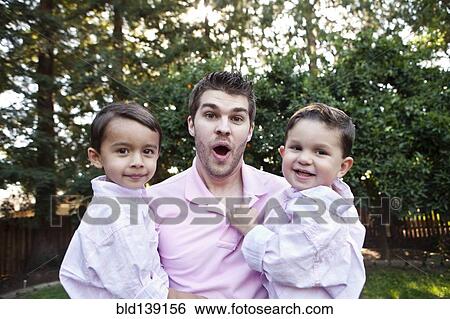 Stock Photograph - Caucasian father holding sons outdoors. Fotosearch