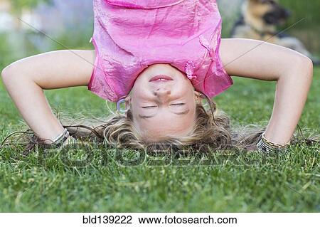 Stock Image - Caucasian girl doing headstand in grass. Fotosearch