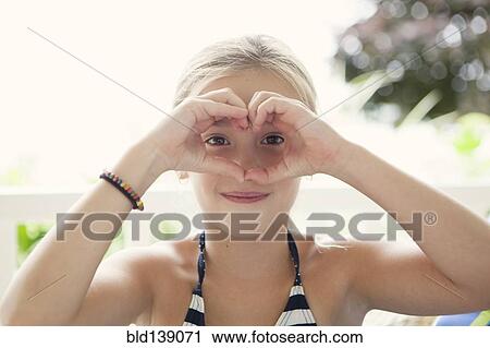 Stock Image - Caucasian girl making heart shape around eyes. Fotosearch