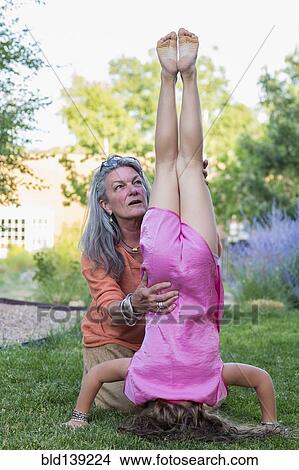Picture - Caucasian grandmother assisting granddaughter with headstand. Fotosearch