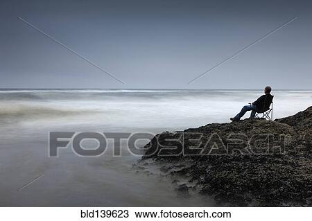 Caucasian man in chair overlooking waves on rocky beach View Large Photo Image Stock Image - Caucasian man in chair overlooking waves on rocky beach. Fotosearch