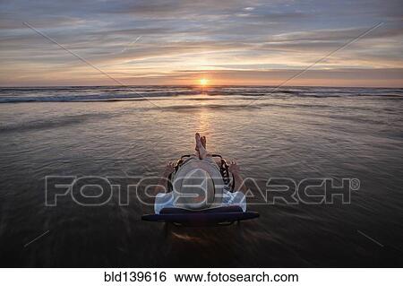 Stock Photograph - Caucasian man in deck chair overlooking sunset on beach. Fotosearch
