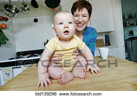 Stock Photograph - Caucasian mother and baby relaxing in kitchen. Fotosearch