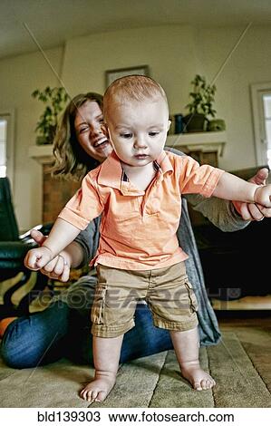 Caucasian mother helping baby walk on living room floor View Large Photo Image Stock Image - Caucasian mother helping baby walk on living room floor. Fotosearch